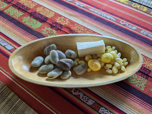 Fava beans, melloco, and corn with fresh cheese Fava beans, melloco (Andean tuber), and corn served with fresh cheese in a wooden bowl.